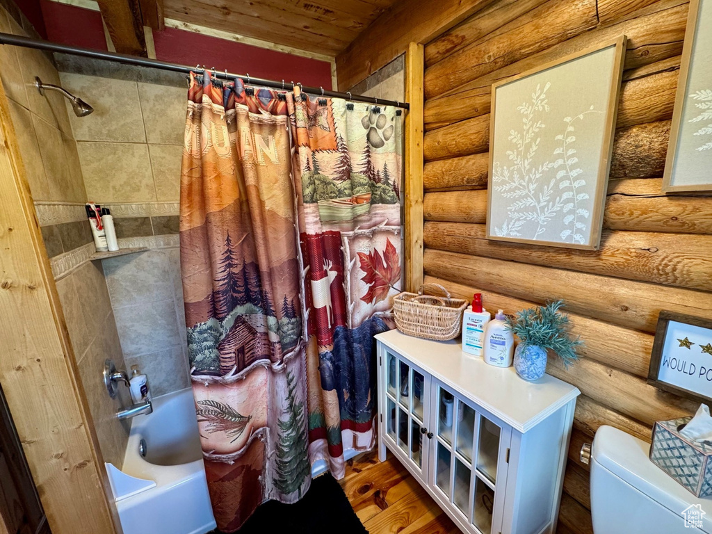 Bathroom featuring log walls, shower / bath combination with curtain, toilet, and wooden ceiling