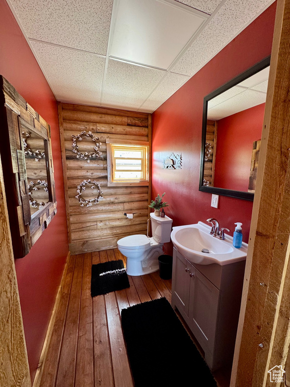 Bathroom featuring rustic walls, toilet, vanity, hardwood / wood-style flooring, and a paneled ceiling