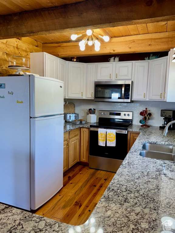 Kitchen featuring appliances with stainless steel finishes, wood ceiling with exposed beams, a sink, light wood-type flooring, and light stone countertops