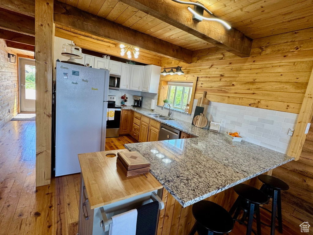 Kitchen with appliances with stainless steel finishes, wood ceiling with exposed beams, a peninsula, light stone countertops, and a sink