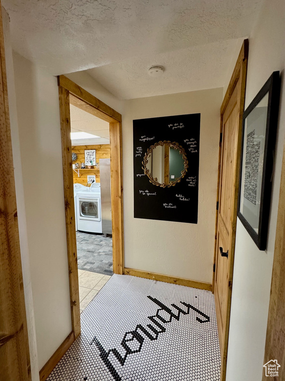 Hall with washer / dryer, a textured ceiling, baseboards, and tile patterned flooring