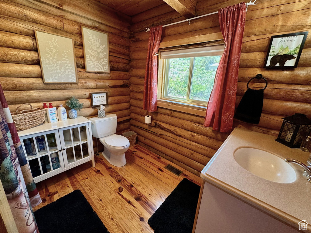 Bathroom featuring toilet, vanity, log walls, and wood finished floors