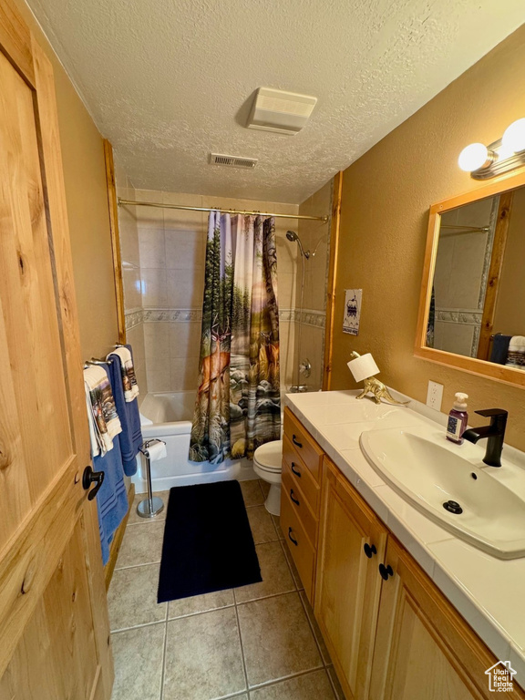 Full bathroom featuring a textured ceiling, vanity, shower / bath combination with curtain, toilet, and tile patterned floors