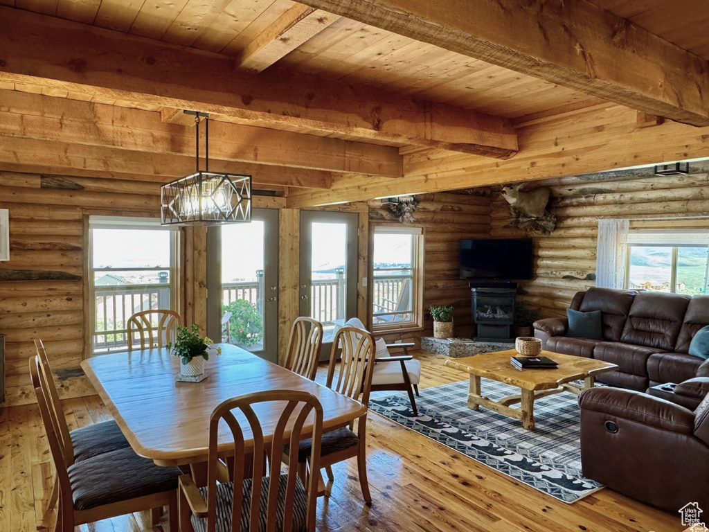 Dining room with log walls, wooden ceiling with exposed beams, light wood-type flooring, and a glass covered fireplace