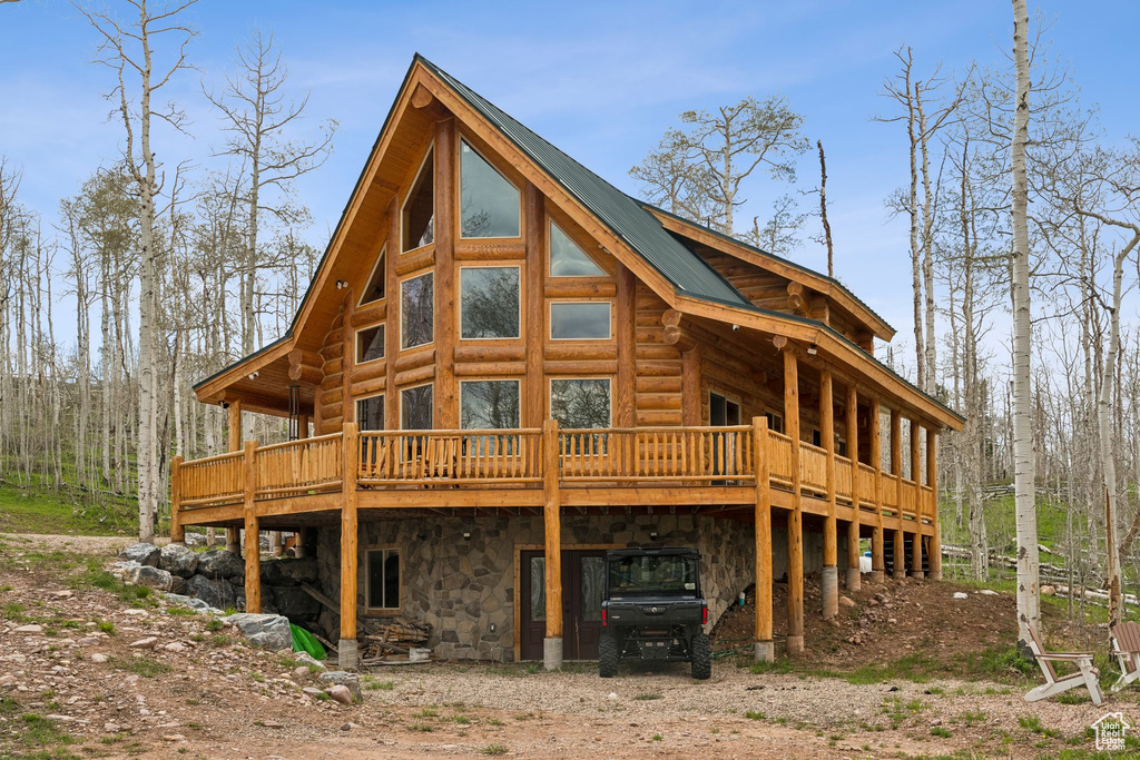 Rear view of property featuring a wooden deck, a carport, dirt driveway, and log exterior