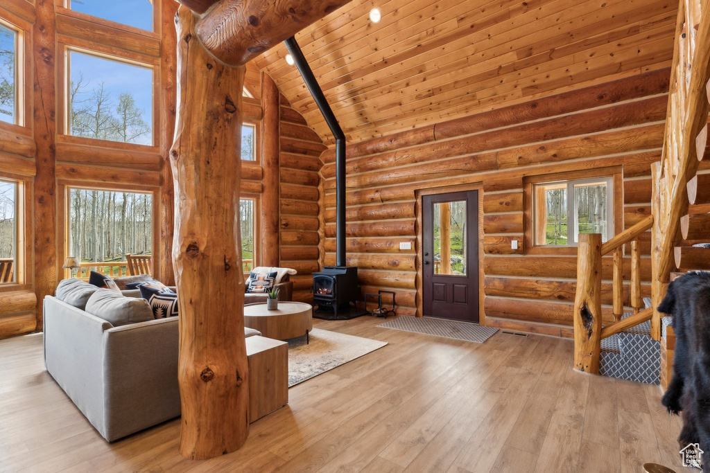 Living area featuring a wood stove, high vaulted ceiling, hardwood / wood-style floors, wooden ceiling, and rustic walls