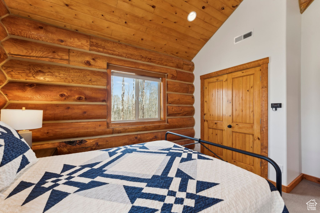 Carpeted bedroom with rustic walls, vaulted ceiling, baseboards, and wooden ceiling