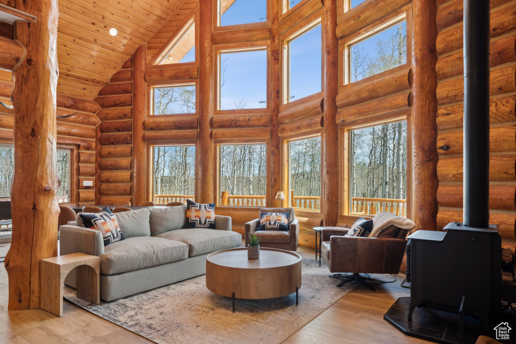 Living area with high vaulted ceiling, a wood stove, rustic walls, wood finished floors, and wooden ceiling