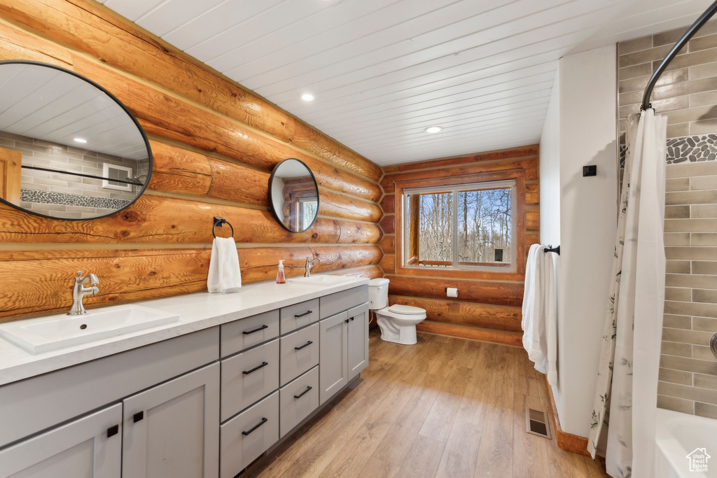Bathroom with double vanity, log walls, toilet, hardwood / wood-style flooring, and recessed lighting