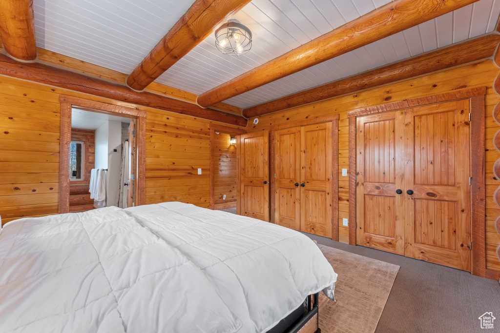Bedroom featuring carpet flooring, wooden ceiling with exposed beams, and wood walls