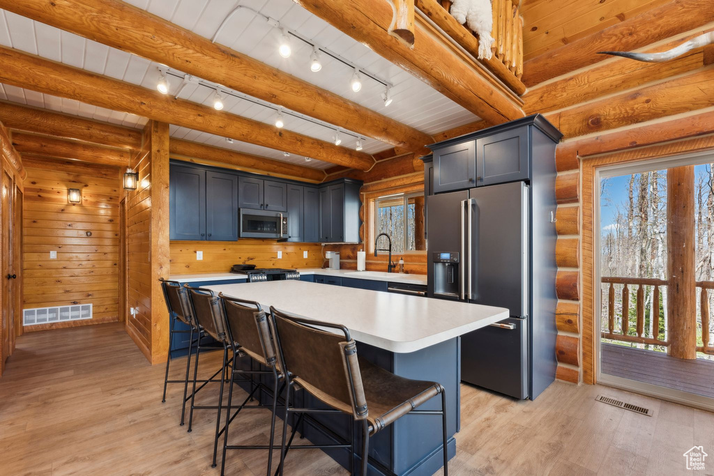 Kitchen featuring appliances with stainless steel finishes, plenty of natural light, light countertops, a kitchen bar, and beam ceiling