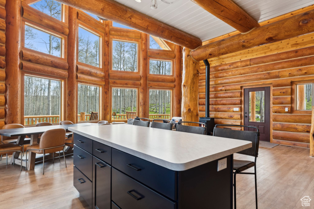 Kitchen with dark cabinetry, light countertops, a wood stove, beam ceiling, and rustic walls