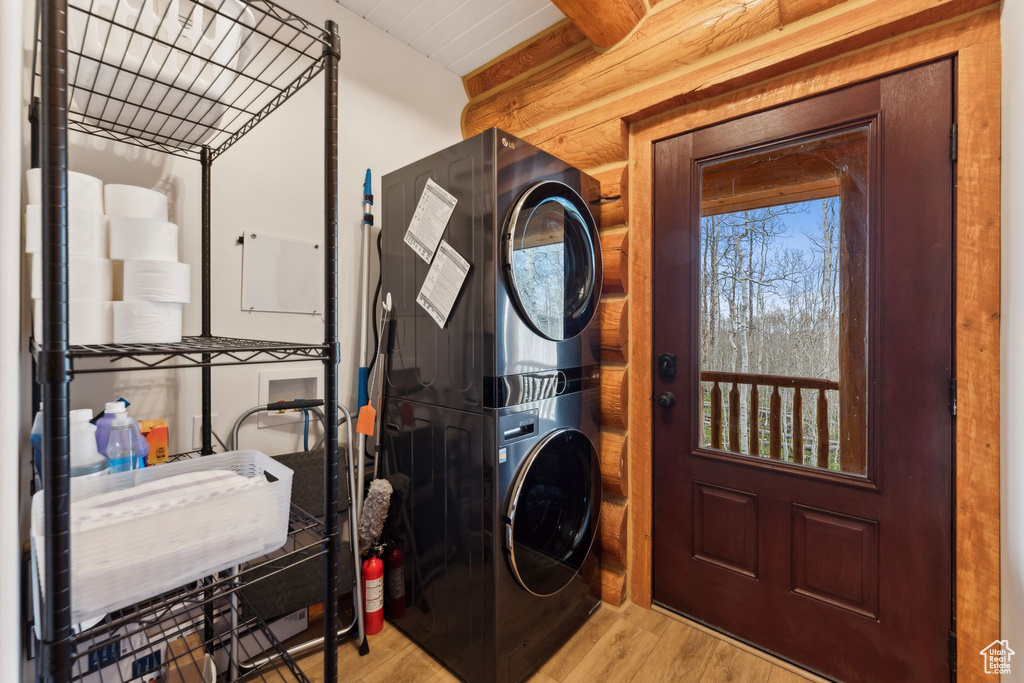 Laundry area with stacked washer / drying machine, wood finished floors, and rustic walls