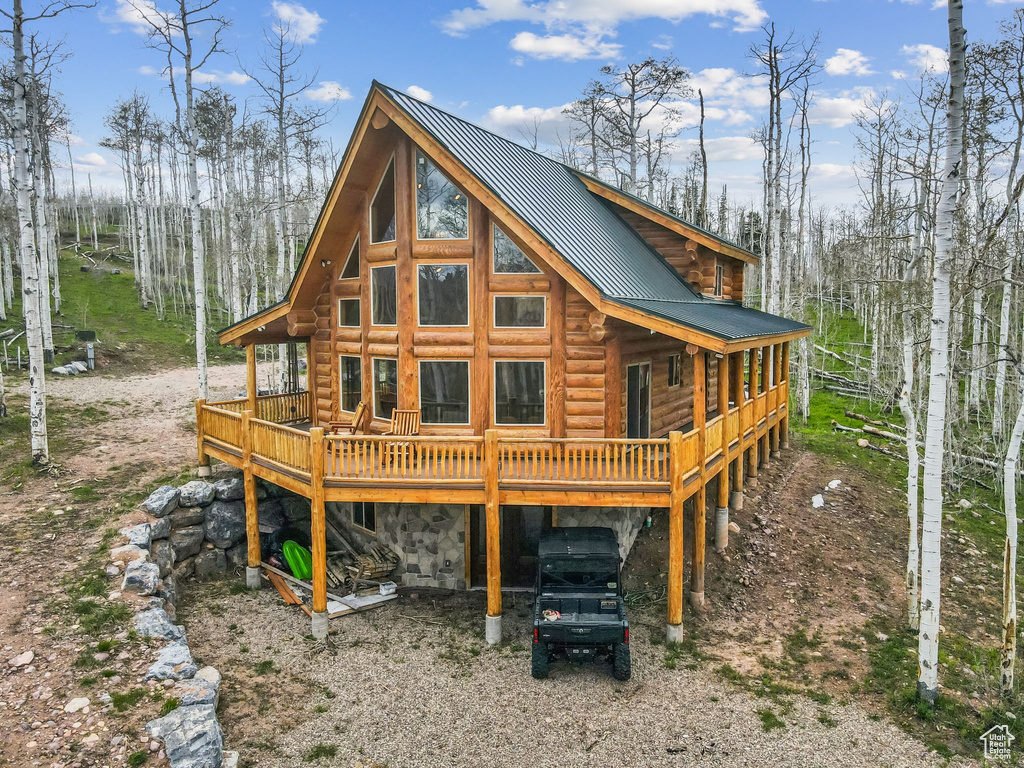 Rear view of property featuring a wooden deck, metal roof, log siding, a carport, and dirt driveway