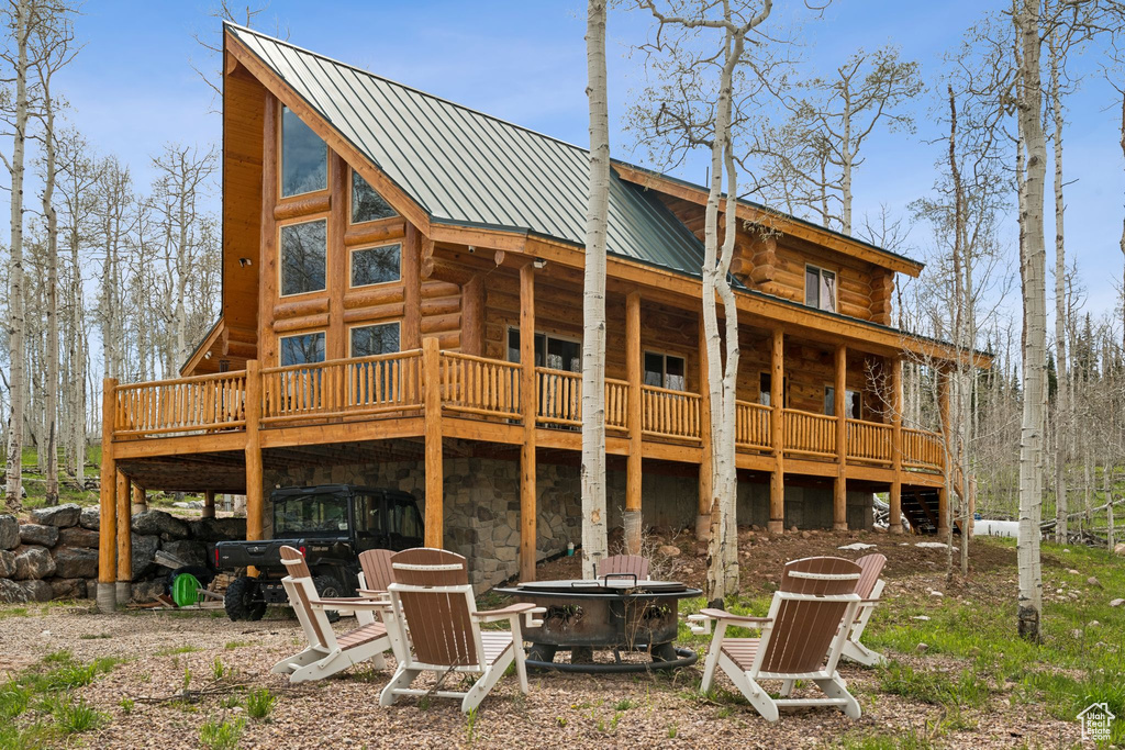 Rear view of property with an outdoor fire pit, log siding, a deck, metal roof, and stone siding