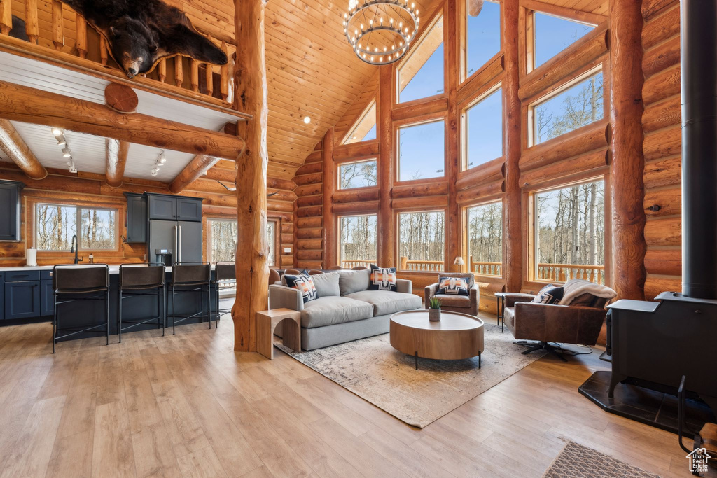 Living room featuring high vaulted ceiling, rustic walls, a wood stove, light wood-style flooring, and a chandelier