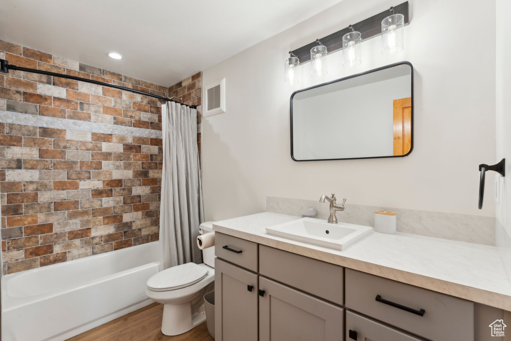 Bathroom featuring vanity, toilet, shower / tub combo, and wood finished floors