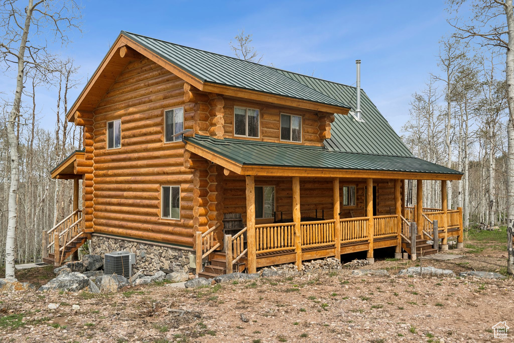 Rear view of property featuring log siding, covered porch, central AC unit, metal roof, and stairway