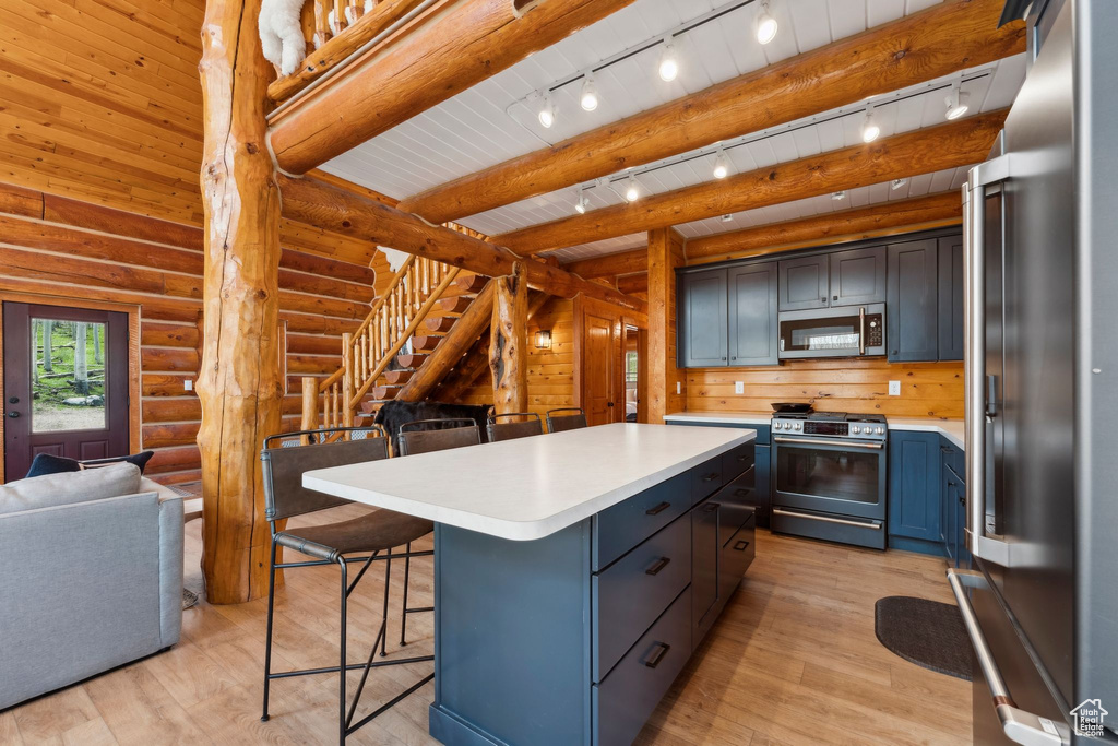 Kitchen featuring appliances with stainless steel finishes, track lighting, a kitchen breakfast bar, light countertops, and light wood finished floors