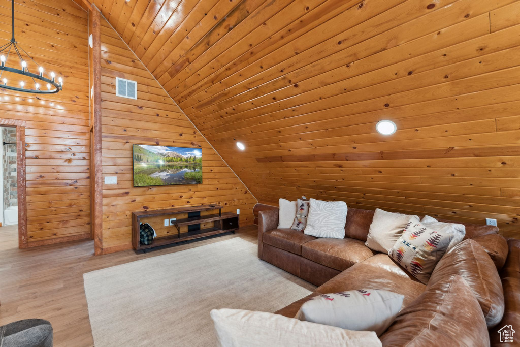 Living room with vaulted ceiling, a chandelier, wooden ceiling, wood finished floors, and wooden walls