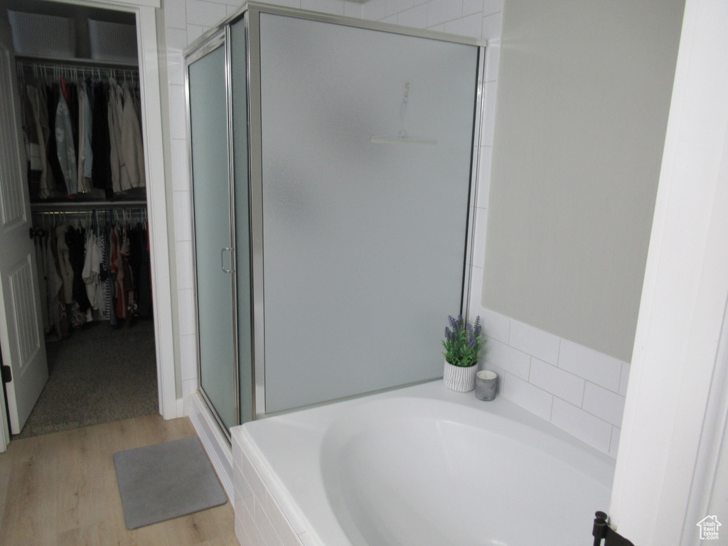 Full bath with a stall shower, a garden tub, a walk in closet, and wood finished floors