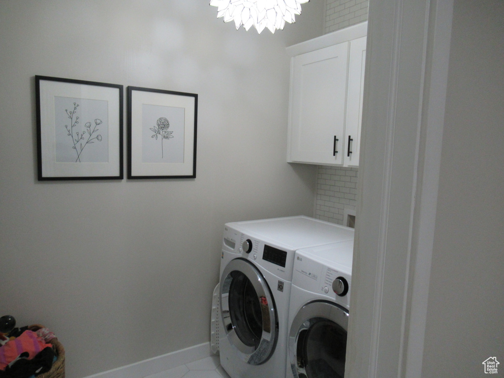 Washroom featuring separate washer and dryer, cabinet space, a chandelier, baseboards, and light tile patterned floors