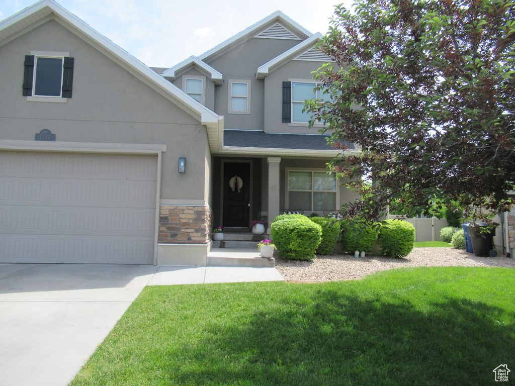 View of front of property with stucco siding, stone siding, driveway, and an attached garage