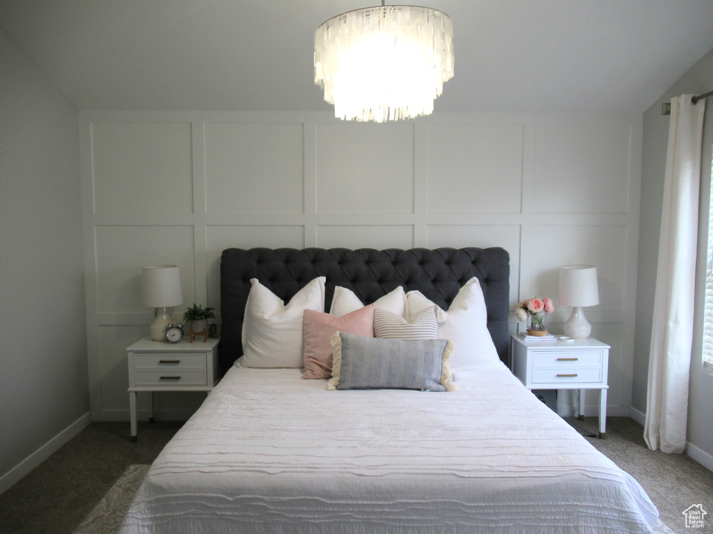 Carpeted bedroom featuring a decorative wall, a chandelier, and baseboards