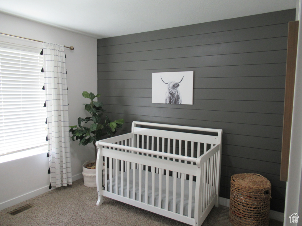 Carpeted bedroom featuring a crib, wooden walls, and baseboards