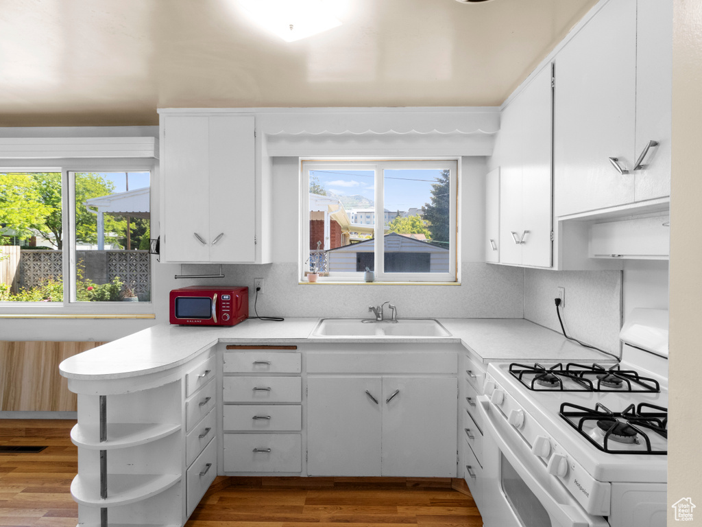 Kitchen with white range with gas cooktop, a sink, open shelves, and plenty of natural light