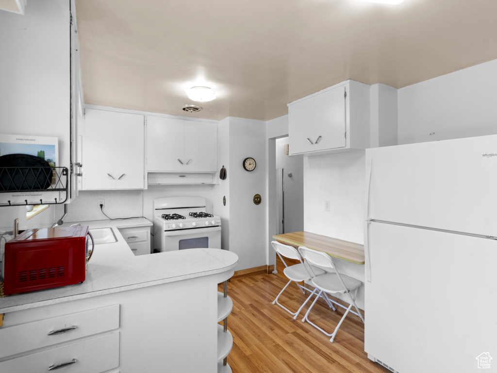 Kitchen featuring white appliances, under cabinet range hood, light countertops, light wood-style flooring, and white cabinets