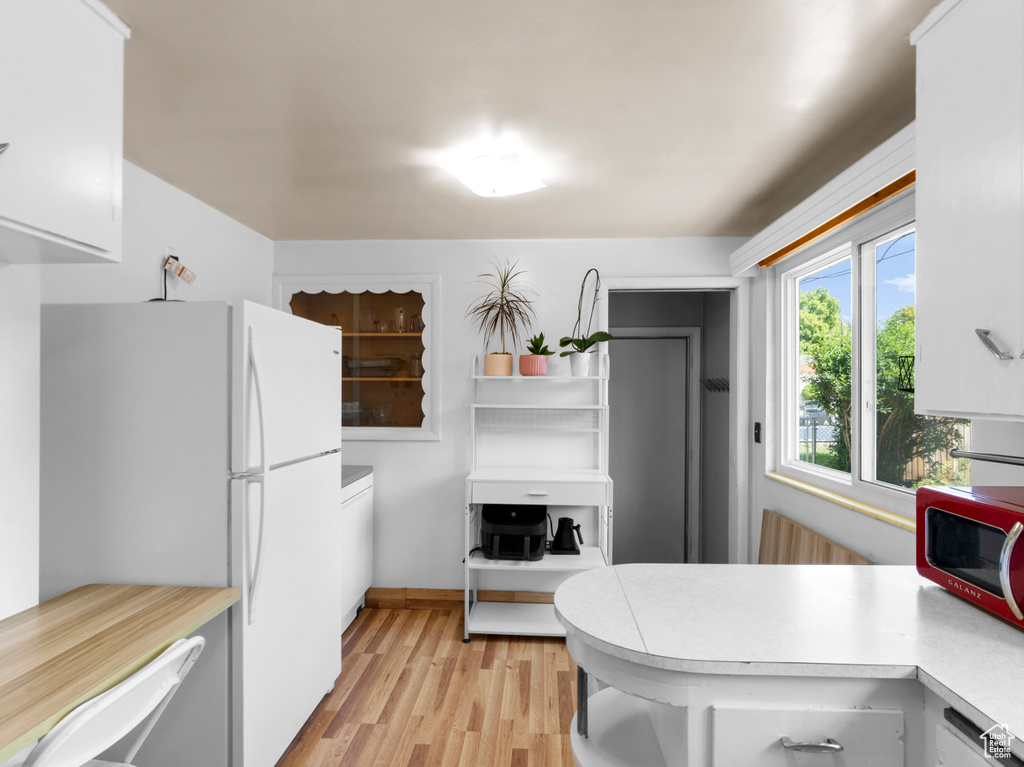 Kitchen with light countertops, light wood-type flooring, a peninsula, freestanding refrigerator, and white cabinetry