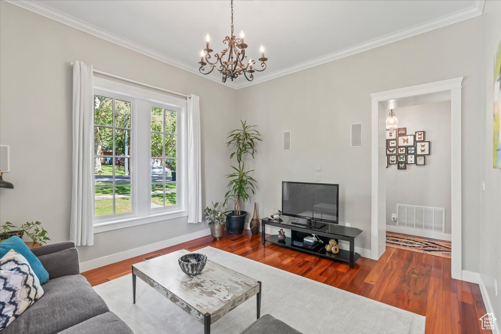 Living room with a chandelier, ornamental molding, baseboards, and wood finished floors