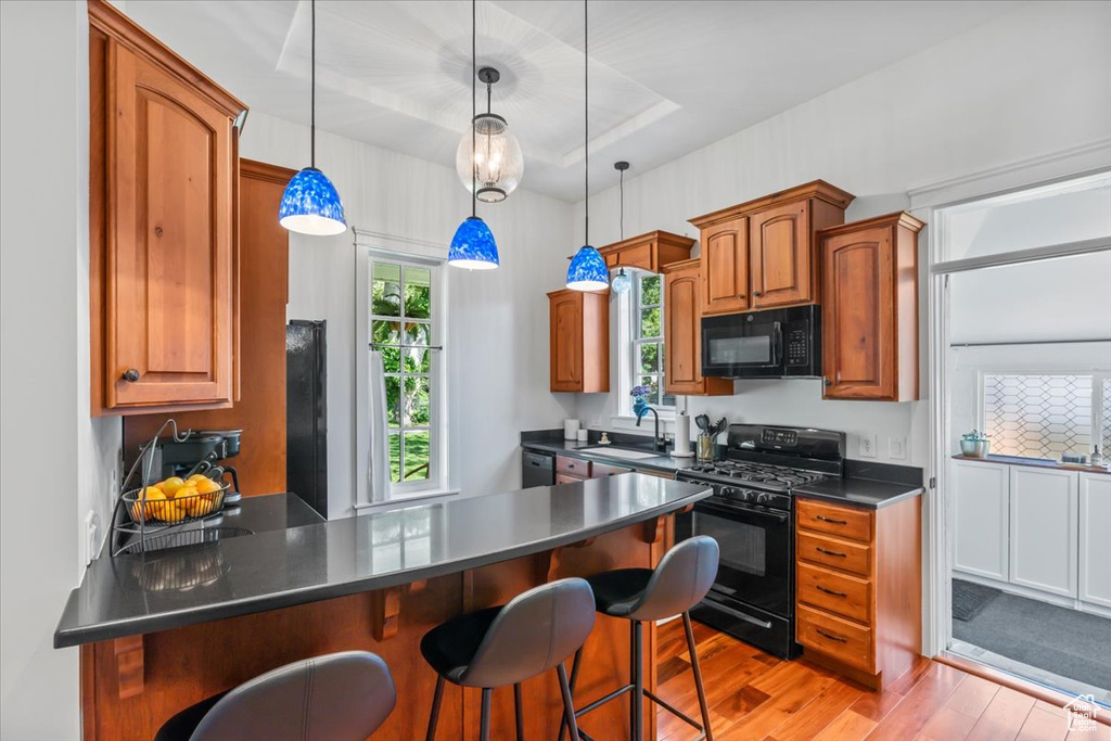 Kitchen with black appliances, light wood-style flooring, a peninsula, dark countertops, and a breakfast bar