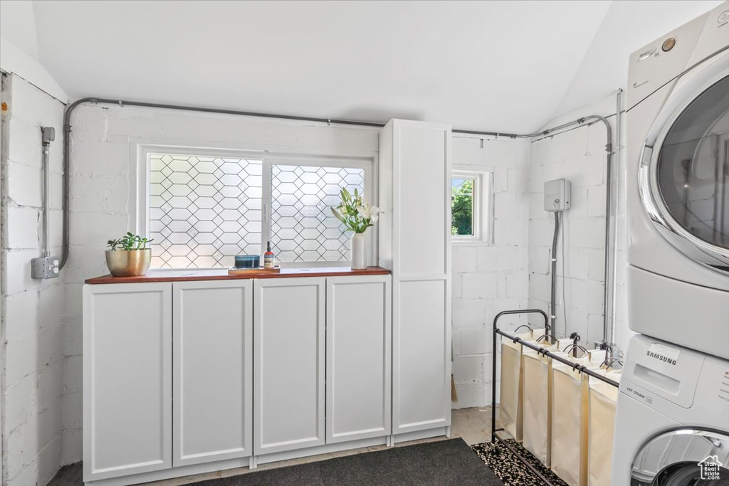 Washroom featuring stacked washing machine and dryer, cabinet space, and concrete block wall