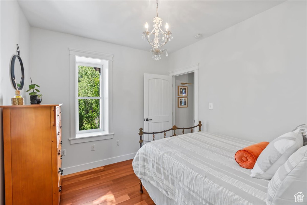Bedroom with multiple windows, wood finished floors, a chandelier, and baseboards