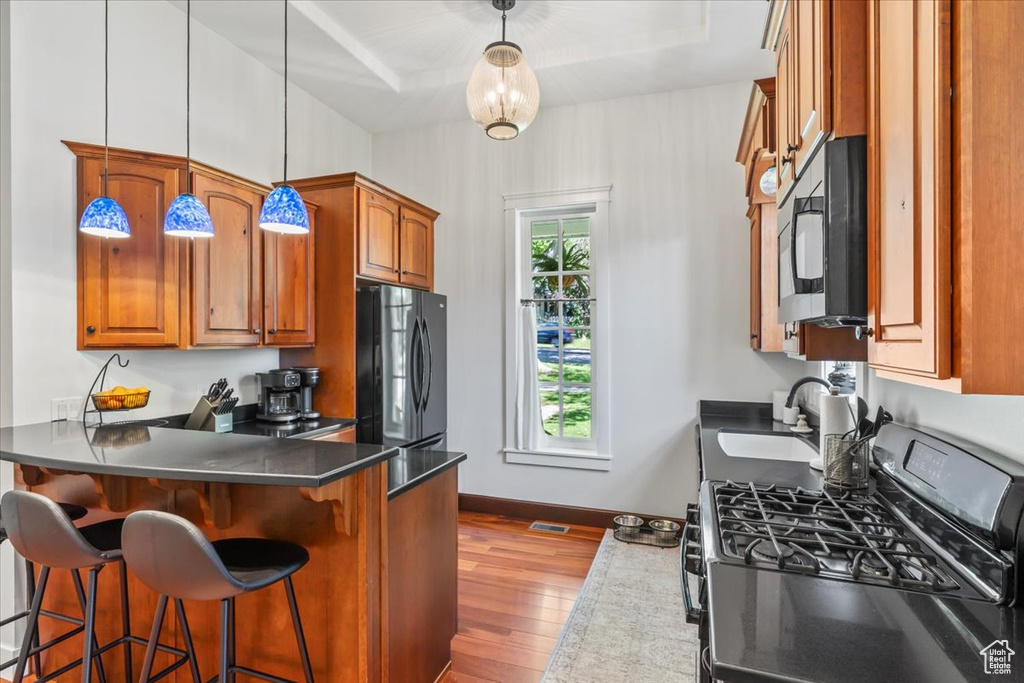 Kitchen featuring black appliances, a sink, dark wood-type flooring, brown cabinetry, and a kitchen breakfast bar