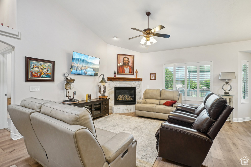 Living area with a ceiling fan, light wood-type flooring, a high end fireplace, lofted ceiling, and baseboards