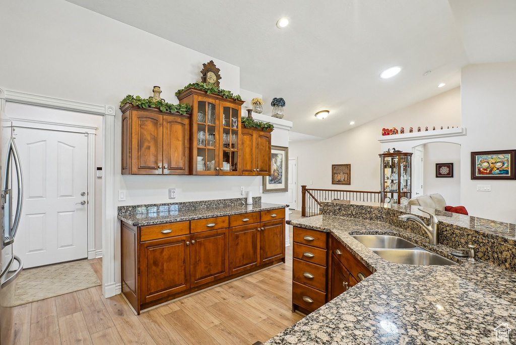 Kitchen with lofted ceiling, a sink, light wood-style flooring, glass insert cabinets, and dark stone countertops