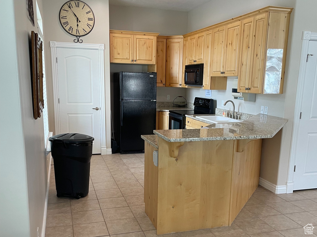 Kitchen featuring black appliances, baseboards, a peninsula, light stone counters, and light brown cabinets