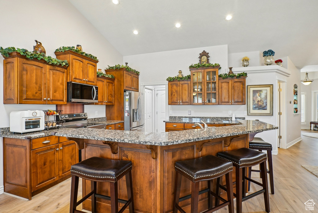 Kitchen featuring appliances with stainless steel finishes, glass insert cabinets, light wood-style floors, brown cabinets, and recessed lighting