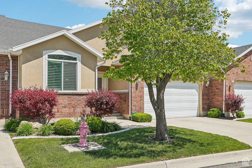 View of front of home with a garage, driveway, a front lawn, brick siding, and stucco siding