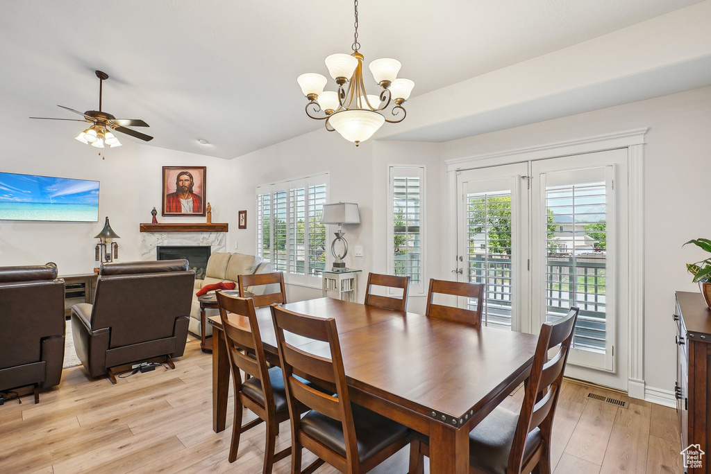 Dining space featuring a fireplace, a chandelier, light wood finished floors, healthy amount of natural light, and vaulted ceiling
