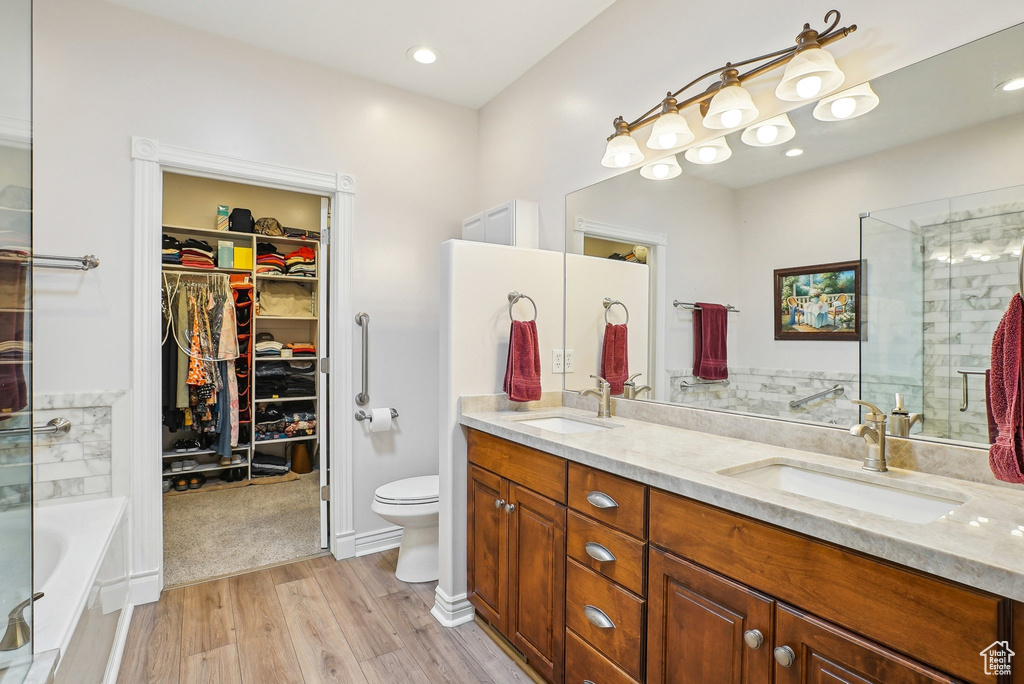 Bathroom with double vanity, toilet, a bath, wood finished floors, and a spacious closet