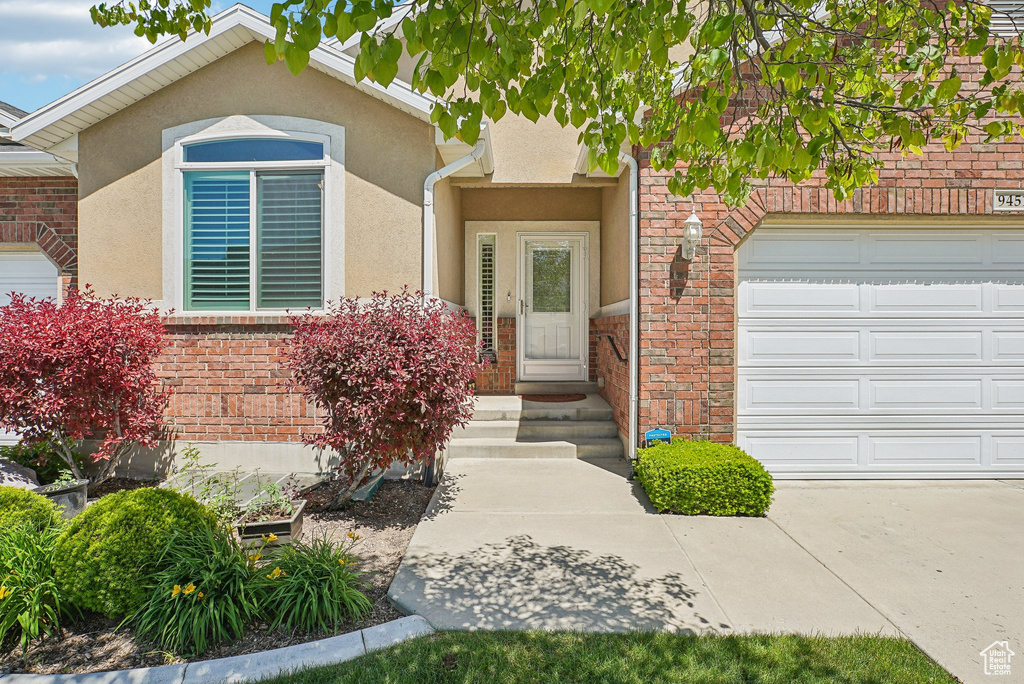 View of exterior entry featuring an attached garage, stucco siding, and brick siding