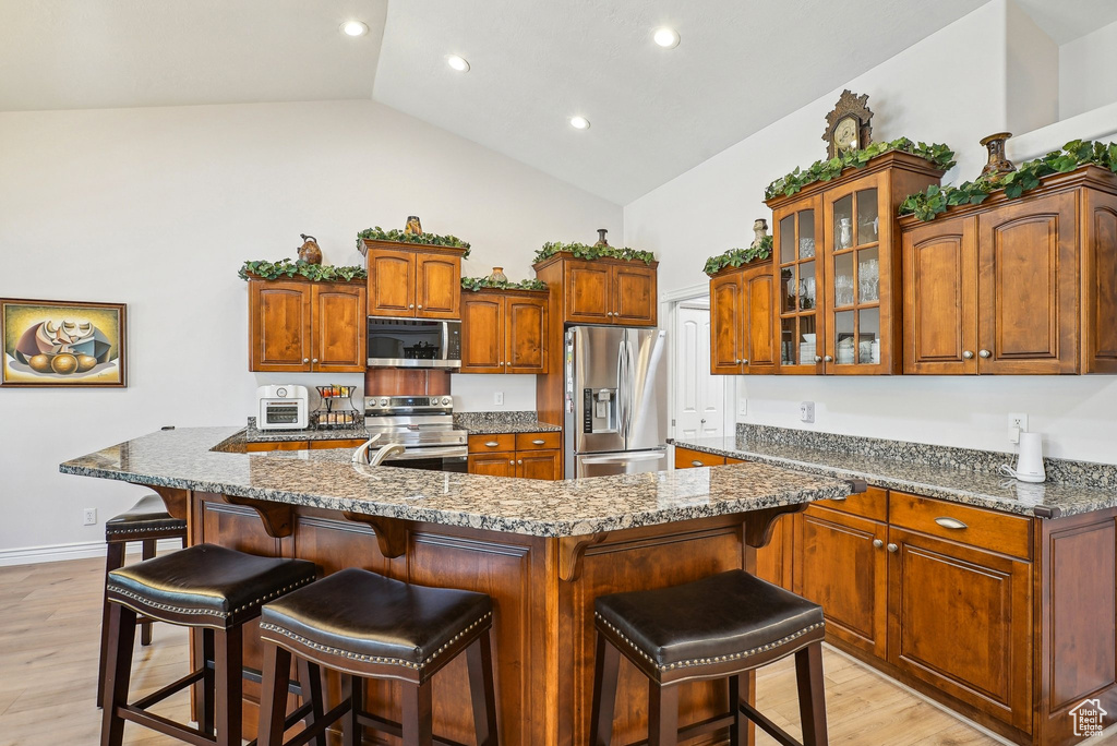 Kitchen featuring stainless steel appliances, light wood-type flooring, glass insert cabinets, a breakfast bar area, and recessed lighting