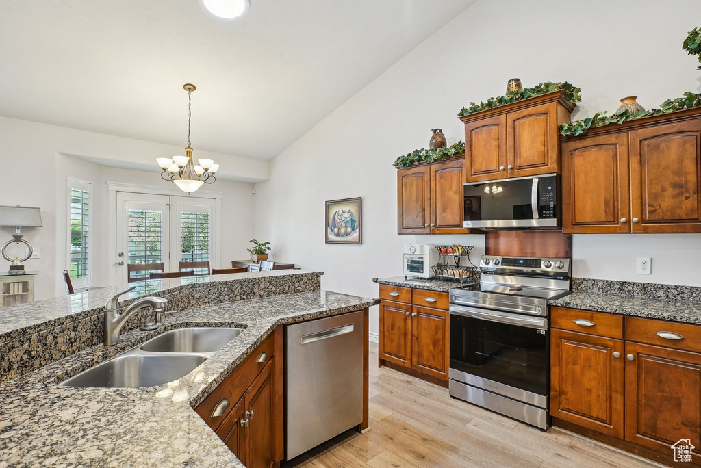 Kitchen with appliances with stainless steel finishes, a sink, vaulted ceiling, light wood-type flooring, and dark stone counters