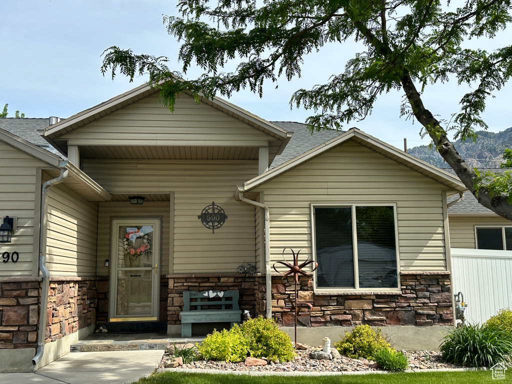 View of front facade with stone siding, covered porch, and a shingled roof