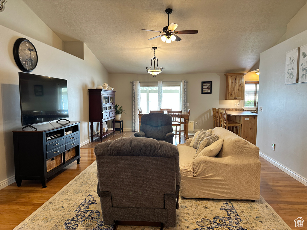 Living area featuring a ceiling fan, vaulted ceiling, wood finished floors, healthy amount of natural light, and baseboards
