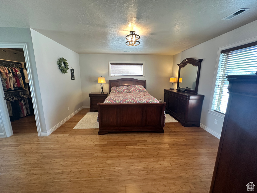 Bedroom featuring a walk in closet, a textured ceiling, light wood-type flooring, and multiple windows